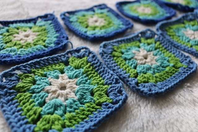Several colorful crochet works-in-progress arranged on a table with yarn and hooks